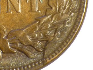 1883 Indian Head Penny cud error showing raised featureless copper blob connected to the rim from die break